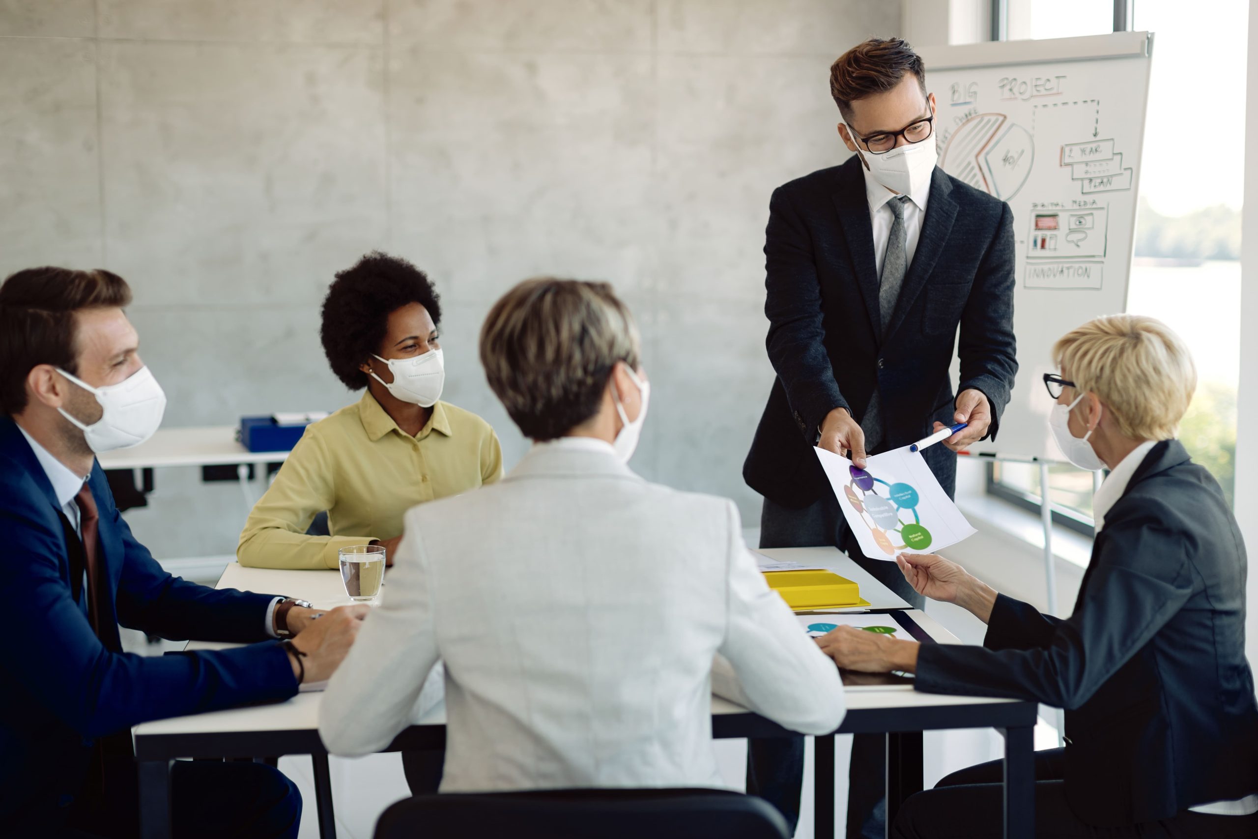young businessman talking his coworkers while analyzing charts meeting board room all them are wearing protective face masks due covid 19 epidemic (1)